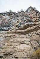 This image showcases a detailed close up of a rugged rocky cliff that towers prominently, with a magnificent mountain visible in the background, enhancing the overall scenic view photo