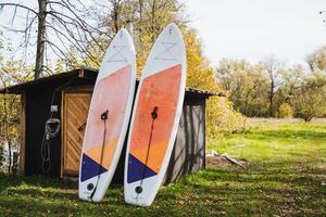 Two colorful surfboards are leaning casually against a small shed in the green grass, surrounded by nature and creating a perfect scene for a fun outdoor day by the water photo