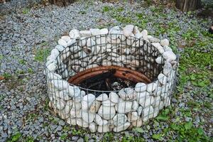 A tranquil outdoor space, a fire pit enclosed by rocks and wire fence, ideal for relaxation and socializing in a peaceful natural setting with elements like grass, wood, and charcoal photo