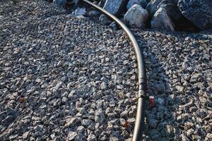 A garden hose is currently laying on top of a large pile of rocks, which may include pebbles, rubble, and soil, creating an interesting scene amidst various terrestrial plants photo