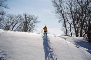 A man stands on the top of a mountain against the background of the sky, the shadow of a skier falls on a snowy slope, a woman is getting ready to slide down the mountain. photo