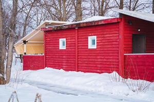 In a picturesque winter landscape, a charming red house stands proudly, enveloped by a blanket of snow and surrounded by tall, majestic trees that add to its serene beauty photo