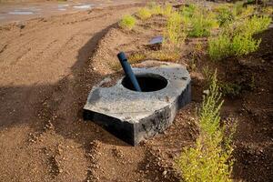 An Abandoned Industrial Site Featuring a Concrete Base and a Pipe, which is Enclosed by Soil and Vegetation photo