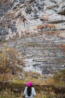 A hiker is admiring the breathtaking and majestic rocky cliffs while exploring the stunning autumn forest during their adventure in nature photo