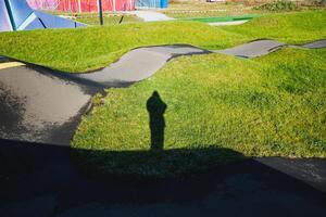 A long shadow of a person is seen standing amidst the tall grass, creating a distinctive silhouette against the backdrop of natures greenery, emphasizing the contrast in the landscape photo