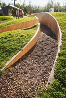 In a serene park setting, a wooden fence is beautifully surrounded by lush green grass and pebbly gravel, providing a charming natural scene for visitors to enjoy and appreciate photo