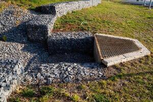 There is a drain located in the grass right next to a set of stairs that leads downwards, providing important water drainage and preventing pooling in the surrounding area photo