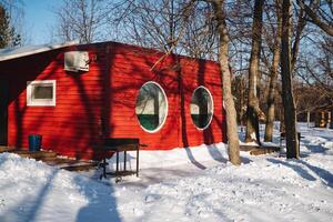 A vibrant red house with charming round windows contrasts beautifully with fluffy white snow, creating a picturesque winter scene that captivates the eye and sparks imagination photo