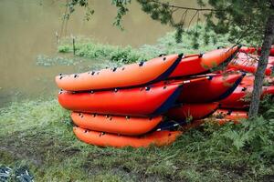 A group of orange kayaks is neatly stacked by a serene lake in a forested area, perfect for outdoor adventure and relaxation surrounded by the beauty of nature photo
