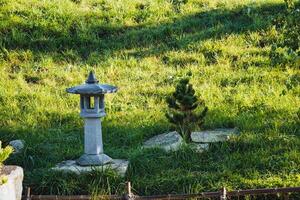 In the center of a lush grassy field, there is a beautifully crafted stone lantern, standing quietly among the vibrant greenery that surrounds it, creating a serene natural landscape photo