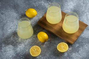 Three glass cups with fresh lemon juice on a wooden board photo