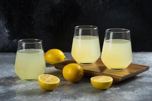 Three glass cups with lemon juice on a wooden board photo