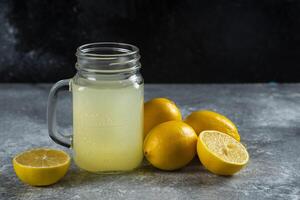 A glass jar of tasty lemon juice and slices on a marble background photo