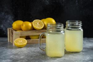 Two glass jars of delicious lemon juice and slices on a marble background photo