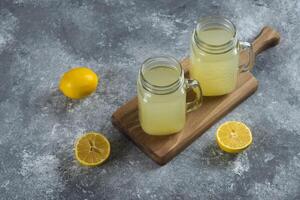 Two glass jars of lemon juice and slices on a wooden board photo