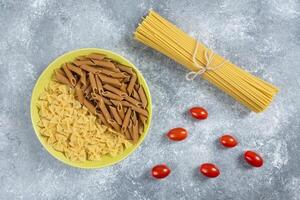 Two types of raw pasta on plate with tomatoes and spaghetti photo
