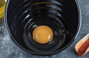 Making breakfast. Raw egg in black bowl. Close up photo