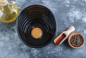 Olive oil and spices. Raw egg in black bowl photo
