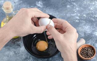 Man hands breaking eggs in bowl over grey background photo