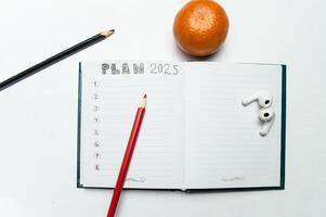 a notebook and an inscription plans for 2025, several pencils and a tangerine. High quality photo