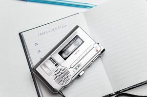 A tape recorder with buttons is on a notebook labeled investigation. the white background and workspace of the student detective professor. High quality photo