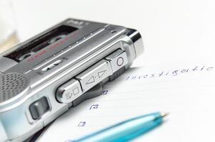 A tape recorder with buttons is on a notebook labeled investigation. the white background and workspace of the student detective professor. High quality photo