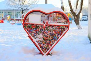 A vibrant and colorful heart sculpture stands prominently in a snowy playground area photo