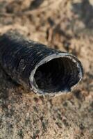 A CloseUp View of a Weathered and Aged Pipe Sitting on Sandy Ground with Surroundings photo