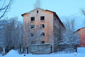 A Desolate, Abandoned Winter Building Surrounded by Snowy Trees in a Cold Landscape photo