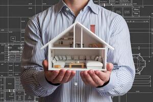 Man holds 3D house model, architectural blueprint backdrop highlights design focus photo