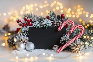 Snow covered pine branches surround black frame with red berries and silver ornaments photo
