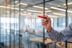 Gloved hand draws red zigzag line on modern transparent graph in office photo