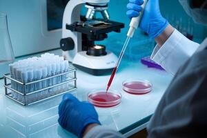 Scientist pipetting red liquid with test tubes and microscope in background photo