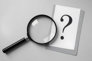 Magnifying glass beside card with question mark in minimalistic monochromatic scene photo