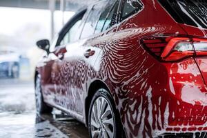 Red car being washed, foam bubbles creating intricate patterns around it photo