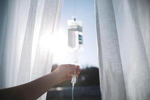 IV bag held before white curtains, soft sunlight emphasizing healing and serene recovery photo