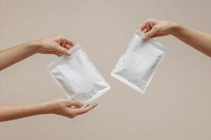 Hands display flat white pouches against beige background, minimalist and clean photo