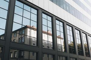 Modern dark facade building, reflective windows contrast old structure in background photo