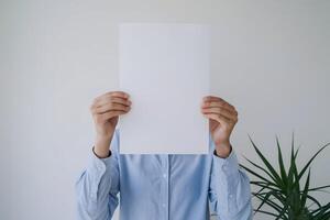 Blank sheet held, obscured face, green plant adds contrast in minimalism photo