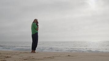 Woman holds her dog on an empty beach, surrounded by clouds on a tranquil, overcast day video