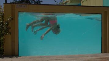 Young girl practicing somersaults underwater in a pool featuring a transparent wall, showcasing skill and enjoyment video