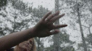 Close-up of a hand drawing mountain shapes on a car window covered with raindrops after rain, blurred trees and cloudy sky in the background, creating a creative and serene atmosphere video