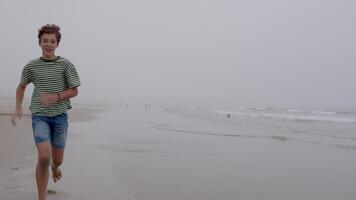 Young boy is running towards the camera on a sandy beach with the ocean and horizon in the background video