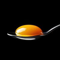 Bright yellow egg yolk resting on a silver spoon against a black background highlighting its texture and color photo