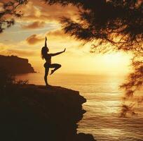 Sunset yoga pose on rocky cliff by the ocean with silhouette of a woman against vibrant colors photo