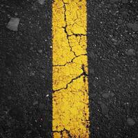 Cracked yellow line on asphalt surface indicating wear and tear on a busy road photo
