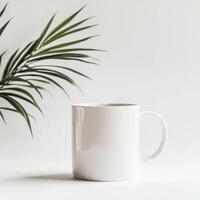 Plain white mug next to green leaf on light background creates a minimalist feel in a cozy setting photo
