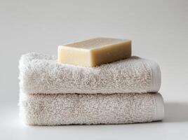 Soft white towels stacked neatly with a bar of soap resting on top in a serene bathroom setting photo