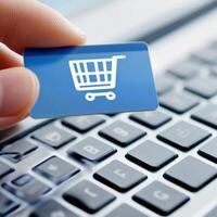Hand holding a shopping cart card above a laptop keyboard in an online shopping setting photo