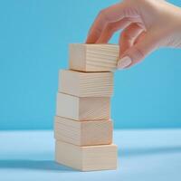 Hand placing wooden blocks on top of each other against a blue background in a creative arrangement photo
